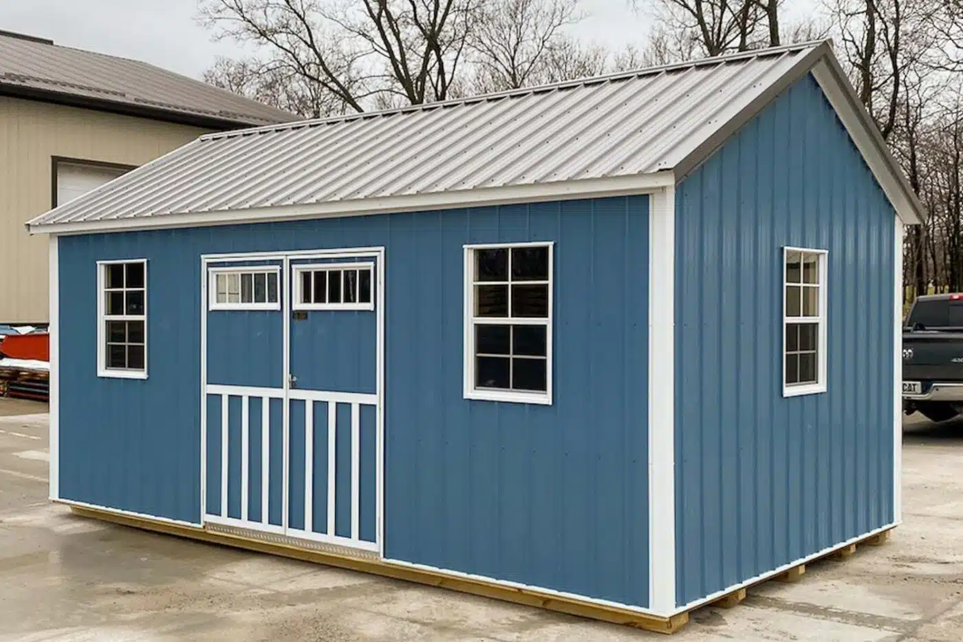 Blue and white metal shed with gray metal roof, double doors, and three windows