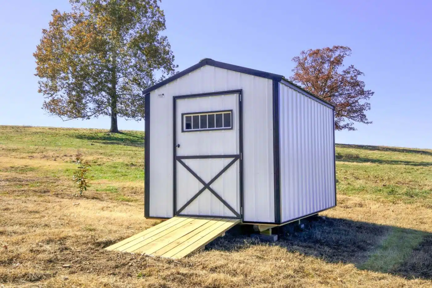 White metal shed with black trim on elevated foundation with wooden ramp