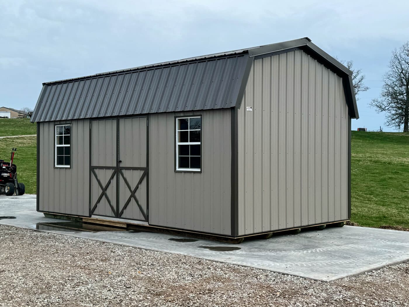 A grey metal barn shed with a dark colored roof and dark trim, two windows and double doors in Missouri